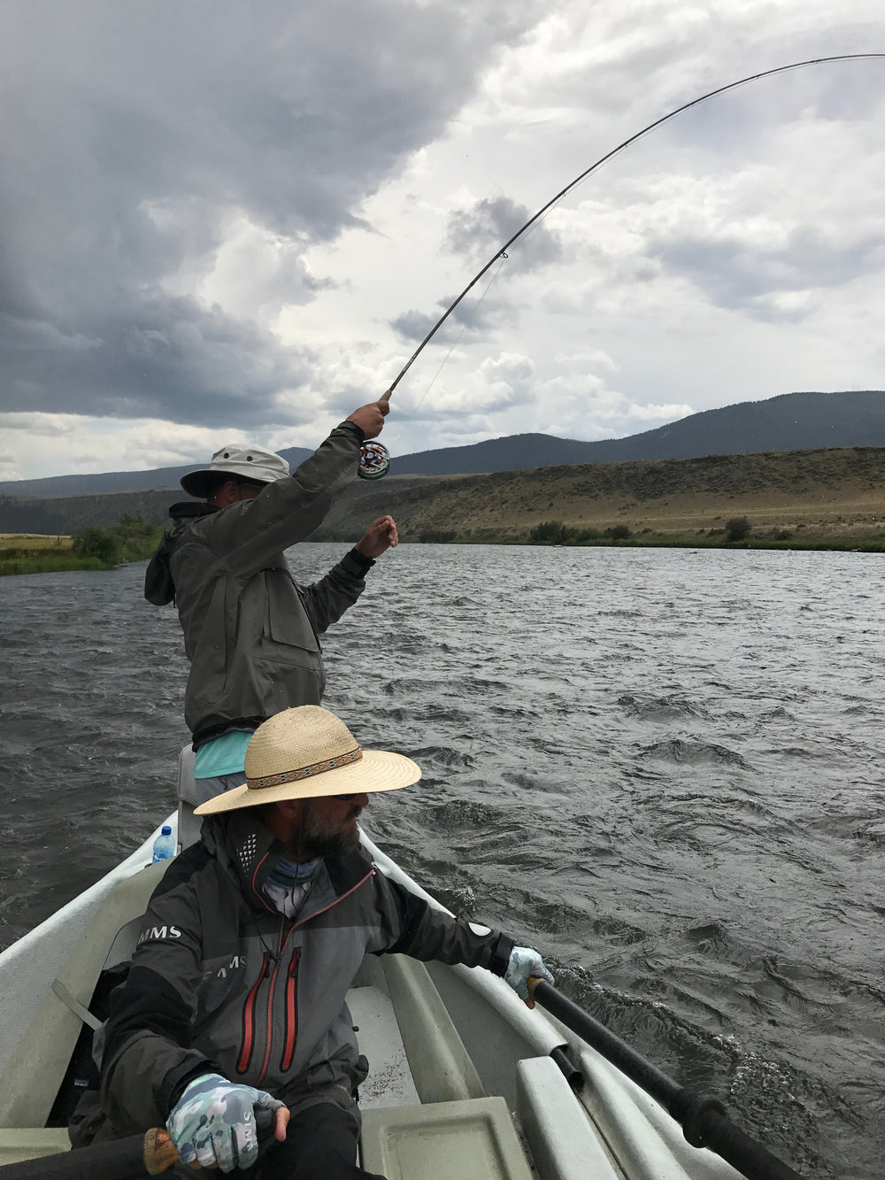 Fish on, guide Brian Rosenberg on the sticks managing the boat to help land this fish while during a float fishing guide trip on the Madison River near Ennis, Montana